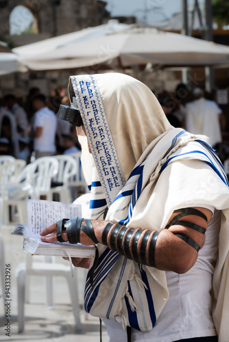 A Jewish man wearing a tallit prayer shawl and tefillin phylacteries prays the morning service holding a siddur at the Western Wall in Jerusalem. photo