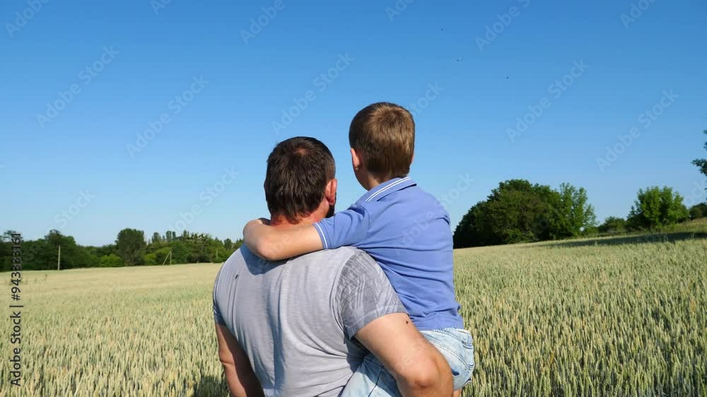 Young daddy holding his little son in arms and looking at wheat field. Dad and his child resting at barley meadow. Happy family enjoy to spending time together at nature. Close up Slow motion Young daddy holding his little son in arms and looking at wheat field. Dad and his child resting at barley meadow. Happy family enjoy to spending time together at nature. Close up Slow motion