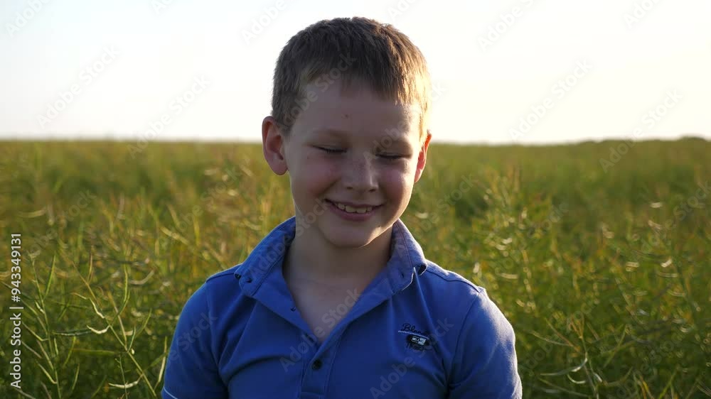 Little smiling boy with freckles looks into camera against background of green field. Portrait of happy child standing in meadow. Close up emotions of small kid with positive expression on face Little smiling boy with freckles looks into camera against background of green field. Portrait of happy child standing in meadow. Close up emotions of small kid with positive expression on face