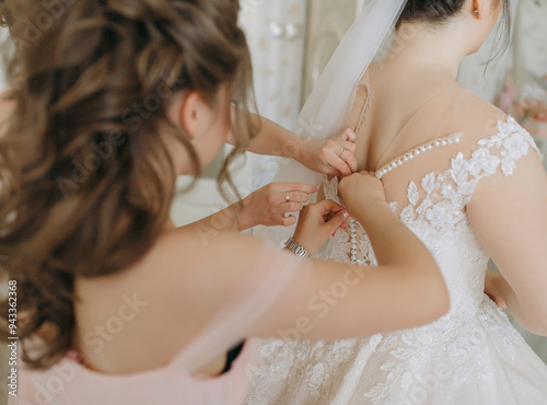 A woman is getting her dress altered by another woman. The bride is wearing a white dress with a pearl necklace