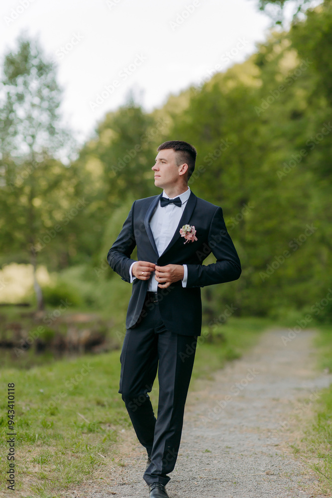 A man in a black suit and white shirt is walking on a path. He is wearing a pink flower on his lapel A man in a black suit and white shirt is walking on a path. He is wearing a pink flower on his lapel