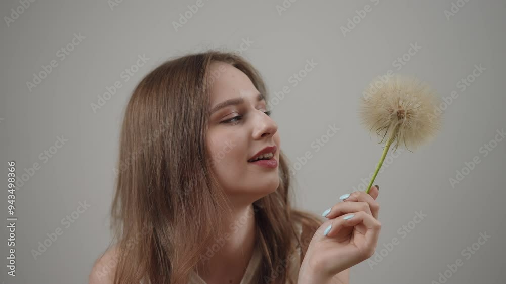 A smiling young woman with a dandelion in hand radiates joy and playfulness against a minimalistic backdrop A smiling young woman with a dandelion in hand radiates joy and playfulness against a minimalistic backdrop