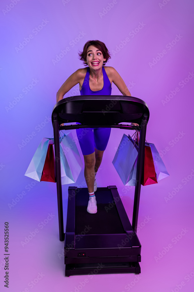 Photo of joyful sporty girl running fast on treadmill shopaholic buying on sport sales isolated ultraviolet color background Photo of joyful sporty girl running fast on treadmill shopaholic buying on sport sales isolated ultraviolet color background