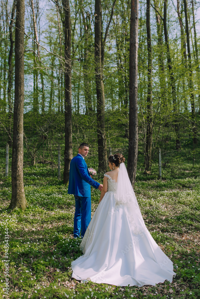 A bride and groom stand in a forest, surrounded by trees and flowers. The bride is wearing a white dress and the groom is wearing a blue suit. They are holding hands and smiling, looking happy A bride and groom stand in a forest, surrounded by trees and flowers. The bride is wearing a white dress and the groom is wearing a blue suit. They are holding hands and smiling, looking happy