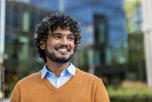 Fotografía Confident Indian businessman smiling in urban environment, wearing orange sweater and blue shirt