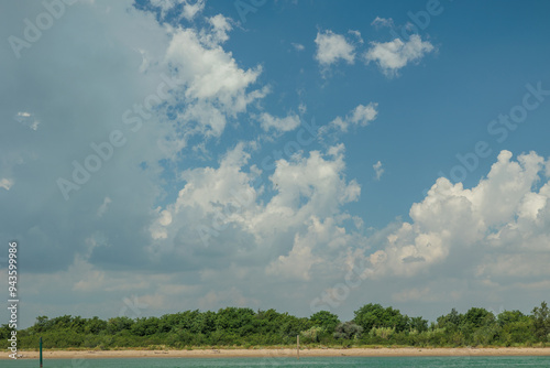 Obraz na płótnie vista dettagliata di una piccola porzione di costa, con una spiaggia e un bosco verde, sotto un cielo azzurro, parzialmente nuvoloso, di giorno, in estate w salonie