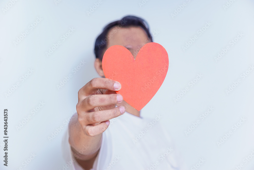 A person holds up a red heart-shaped cutout, symbolizing love and affection against a clean white background. World Heart Day concept A person holds up a red heart-shaped cutout, symbolizing love and affection against a clean white background. World Heart Day concept