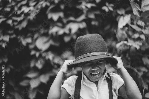A boy pulls his hat on his head with his hands and laughs