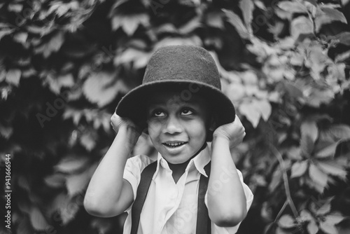 A boy holds his hat on his head with his hands, looking up