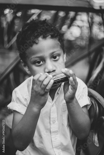 A boy sits on a wooden chair and plays the harmonica