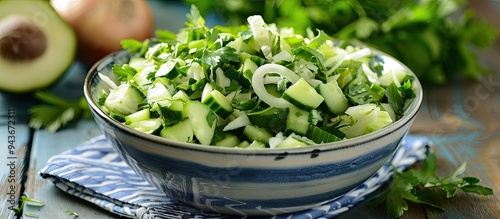 Green vegetable salad made of cabbage cucumbers and spring onion in a blue bowl accompanied by a napkin and ingredients on a white wooden table. with copy space image. Place for adding text or design