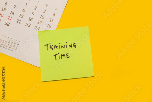 Concepto de tiempo de entrenamiento escrito en un post it junto a un calendario sobre un fondo amarillo. Vista superior y de cerca. Copy space