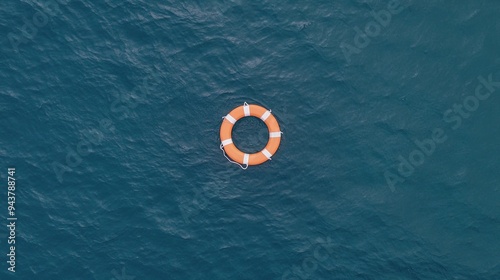 An orange life preserver drifts gently on the calm sea during a clear day, surrounded by a vast expanse of water and a bright blue sky filled with fluffy clouds