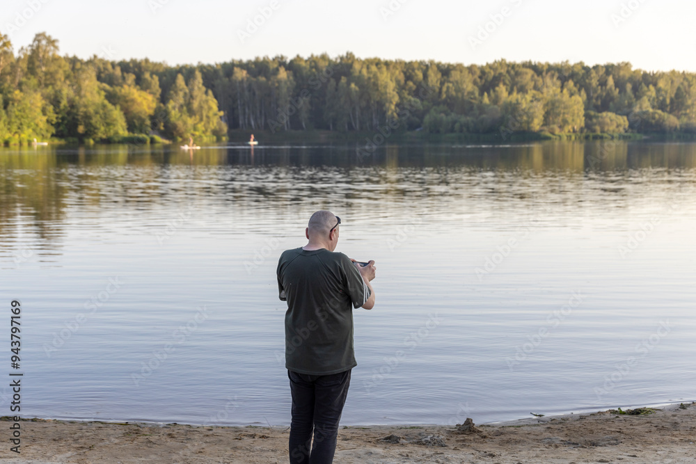 Fototapeta premium A man is standing on a beach, taking a picture of the lake