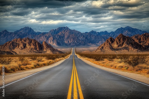 A long straight road in the desert with mountains in the background.