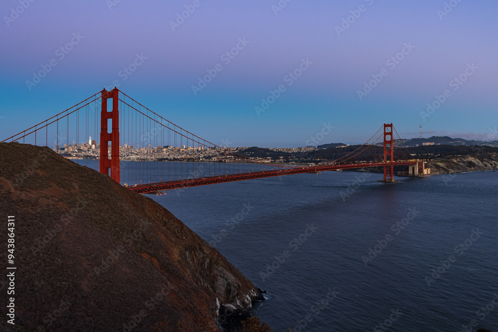 View of golden gate bridge in california during dusk, in a summer evening, with san francisco lights in the background, united states. View of golden gate bridge in california during dusk, in a summer evening, with san francisco lights in the background, united states.