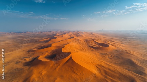 A bird's-eye view of a vast desert landscape, with rolling sand dunes stretching out into the horizon under a deep blue sky, evoking a sense of solitude