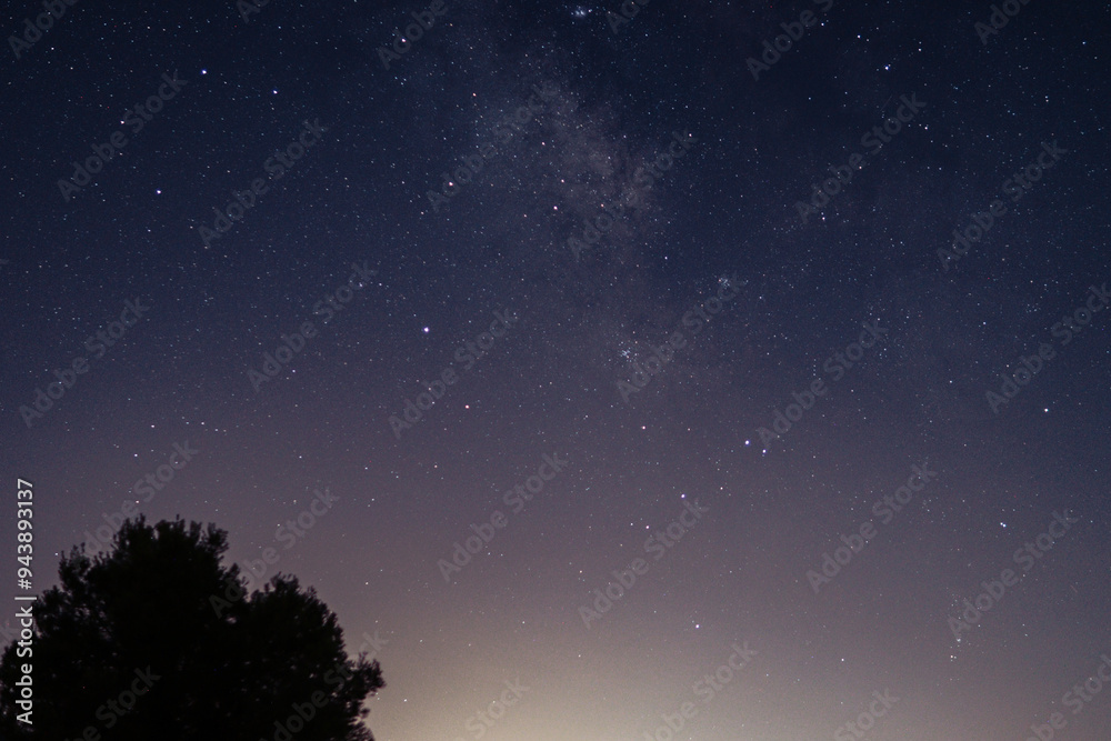 The milky way galaxy stretches across starry night sky with gradient of dark blue, purple, and orange completing scene
