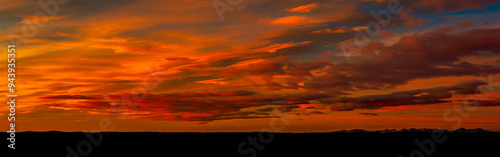 Panoramic of colorful red and orange cloud formations creating a dramatic sky at twilight with a silhouetted horizon; Calgary, Alberta, Canada
