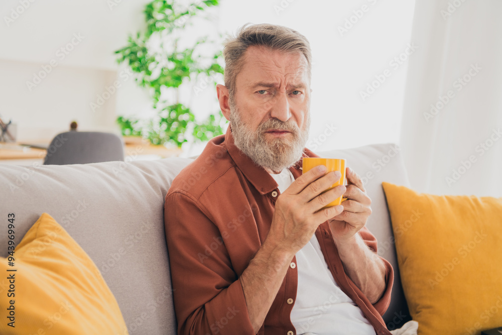 Photo of senior male sit couch sick drink tea mug dressed brown outfit cozy day light home interior living room Photo of senior male sit couch sick drink tea mug dressed brown outfit cozy day light home interior living room