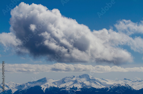 Beautiful cloud formations in a blue sky over snow-capped mountains; Whistler, British Columbia, Canada photo