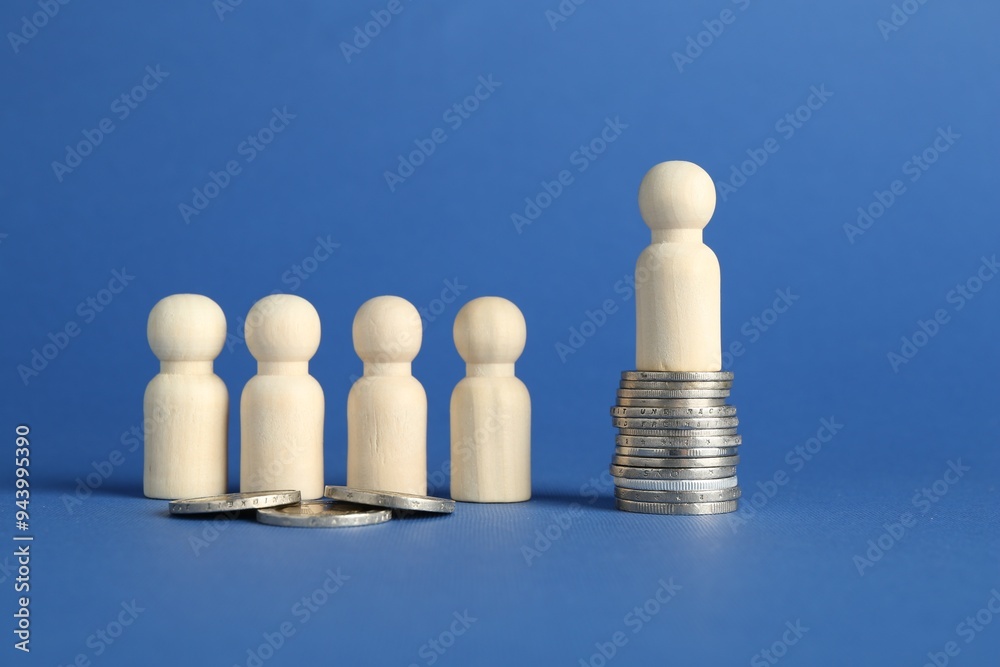 Financial inequality. Wooden figures with uneven amount of coins on blue background Financial inequality. Wooden figures with uneven amount of coins on blue background