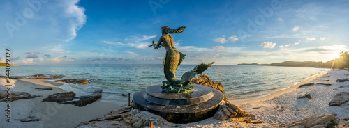Mermaid sculpture in outdoor public sand and rock beach with seascape view at Samet island, Rayong, Thailand, under twilight sunset cloudy sky