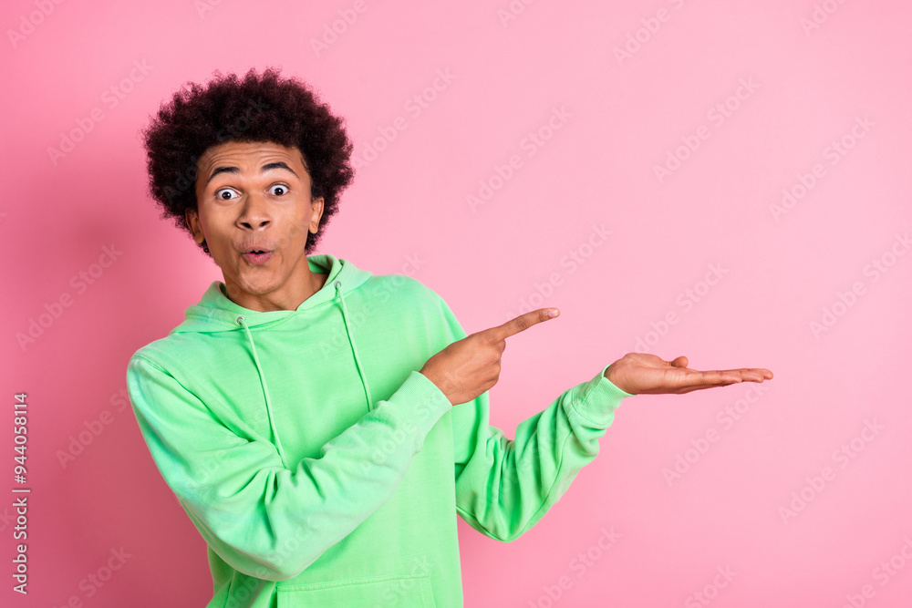 Portrait of cool young man point finger hold empty space wear green hoodie isolated on pink color background Portrait of cool young man point finger hold empty space wear green hoodie isolated on pink color background