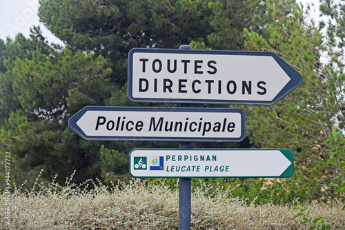 Panneau de signalisation : flèches indiquant toutes directions, police municipale, circuit cycliste vers Perpignan et Leucate plage.