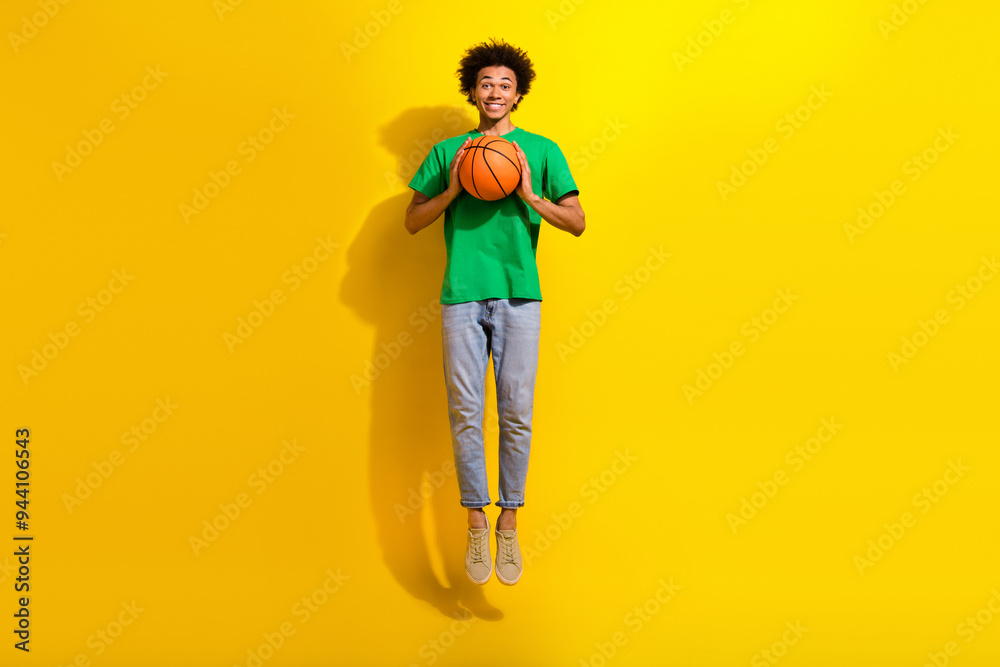 Full length photo of funky cool guy dressed green t-shirt jumping high rising ball emtpy space isolated yellow color background