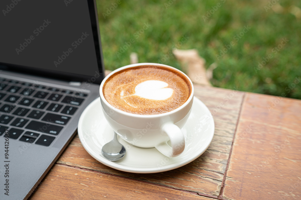 Close-up of Hot coffee latte with latte art milk foam in cup mug and laptop computer on wood desk office desk in coffee shop at the cafe,during business work concept Close-up of Hot coffee latte with latte art milk foam in cup mug and laptop computer on wood desk office desk in coffee shop at the cafe,during business work concept