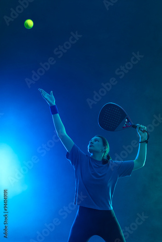 Padel tennis player with racket on tournament. Girl athlete with paddle racket on court with blue neon colors. Sport concept. Download a high quality photo for design of a sports app or tour events. photo