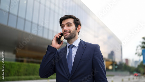 Skilled caucasian project manager calling phone while walking at city with blurred background. Skilled businessman using smart phone talking to project manager with blurred background. Exultant.