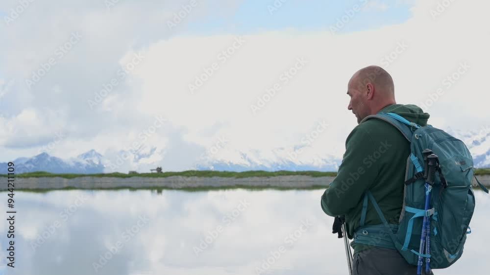 A hiker stands near a reflective lake, gazing at the stunning snow-capped mountains in the distance. The peaceful setting highlights the beauty of nature and outdoor exploration. 4k footage A hiker stands near a reflective lake, gazing at the stunning snow-capped mountains in the distance. The peaceful setting highlights the beauty of nature and outdoor exploration. 4k footage