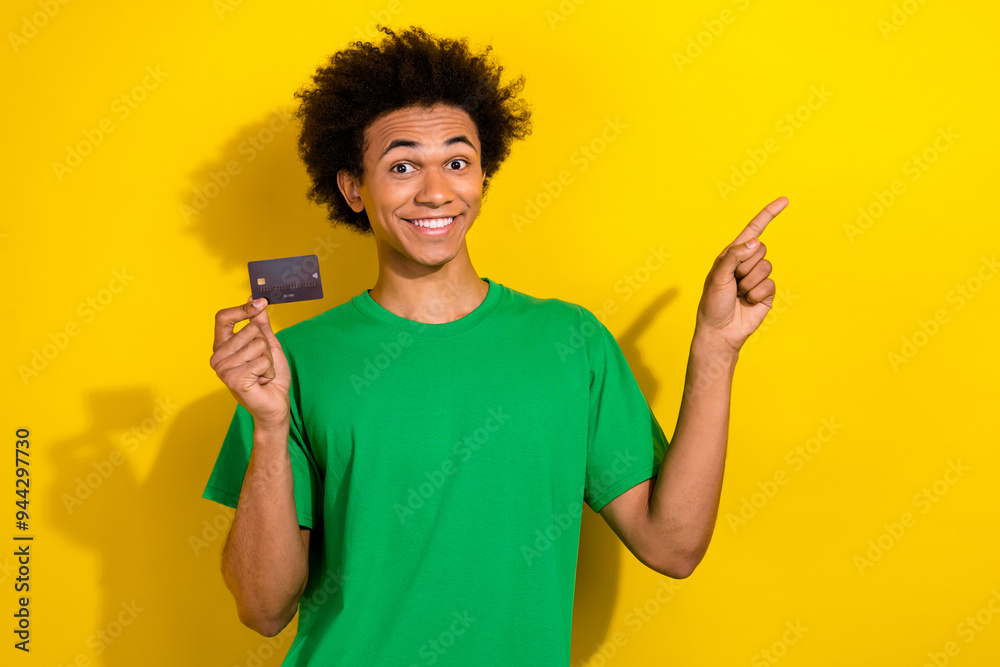 Photo of cheerful positive guy dressed green t-shirt holding bank card pointing emtpy space isolated yellow color background Photo of cheerful positive guy dressed green t-shirt holding bank card pointing emtpy space isolated yellow color background