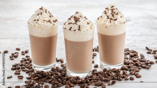 Three tall glasses of iced coffee topped with whipped cream and chocolate shavings, surrounded by coffee beans on a light surface.