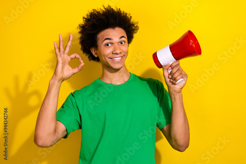 Photo of handsome good mood guy wear green t-shirt risng loudspeaker showing okey emtpy space isolated yellow color background photo