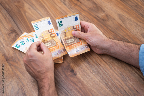 Hands managing 50 euro banknotes on a wooden table. Concept of currency handling, financial organization, and budgeting  photo