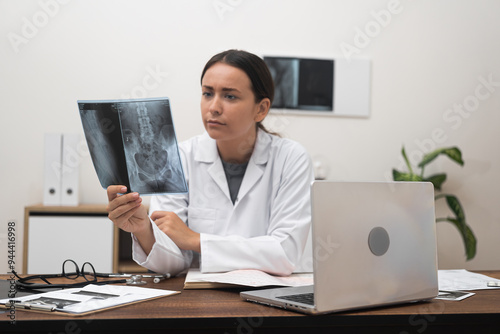 computer-equipped table, an orthopedic doctor examines patient X-ray films scans, showcasing the integration of online medicine