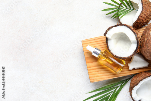 Wooden board with bottle of coconut cosmetic oil and plant leaves on white background