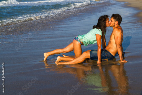 Happy young couple enjoying summer at the beach at dusk, getting wet, breathing fresh air, having fun kissing and teasing one another