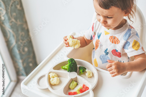 children's plastic plate with vegetables broccoli, cauliflower, cucumbers, tomatoes, child eats