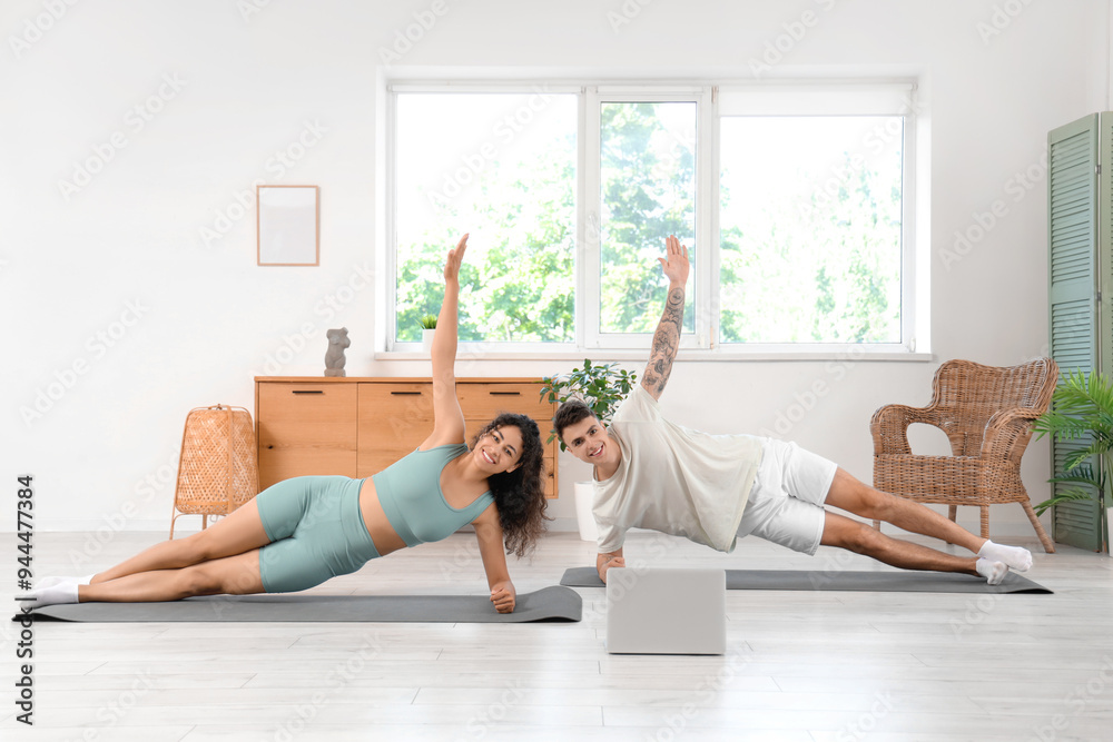 Young couple with laptop practicing yoga together at home Young couple with laptop practicing yoga together at home