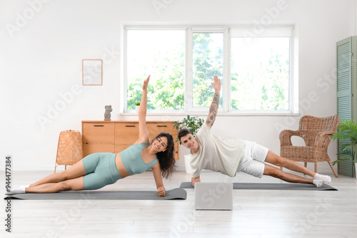 Young couple with laptop practicing yoga together at home