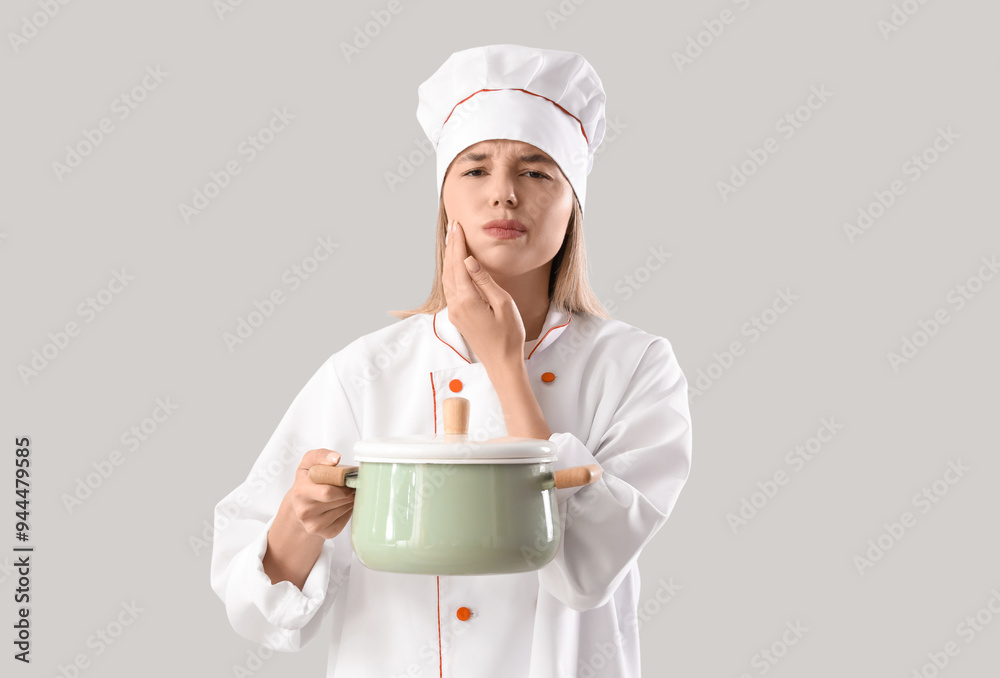 Young female chef with cooking pot suffering from tooth ache on grey background Young female chef with cooking pot suffering from tooth ache on grey background