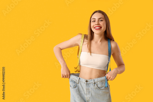 Young woman in loose jeans on yellow background. Weight loss concept