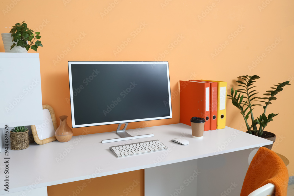 Obraz premium Comfortable workspace with modern computer near orange wall