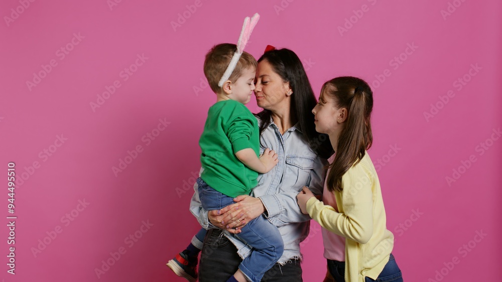 Fototapeta premium Adorable lovely family showing love and laughing on camera, children feeling happy and playful in studio. Mother with a boy and a girl kissing and hugging each other, joyful people. Camera B.