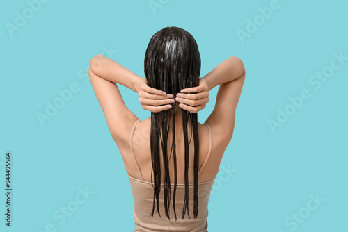 Beautiful young woman applying hair mask on blue background, back view