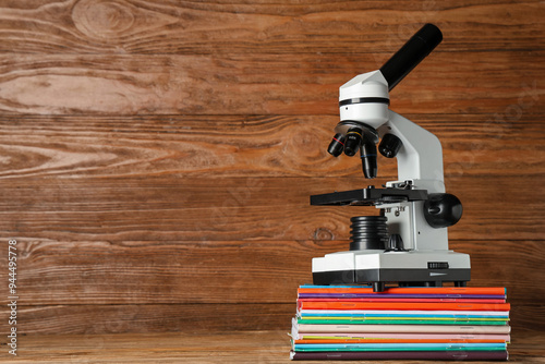 Modern microscope with copybooks on table against wooden background photo